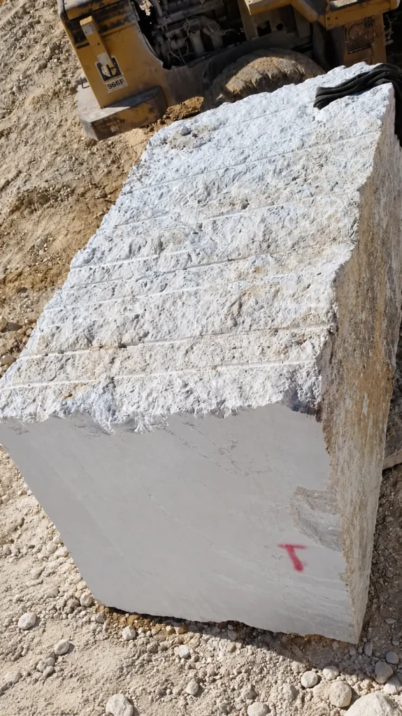 Large rough-cut white natural stone block at a quarry, with a yellow loader in the background.