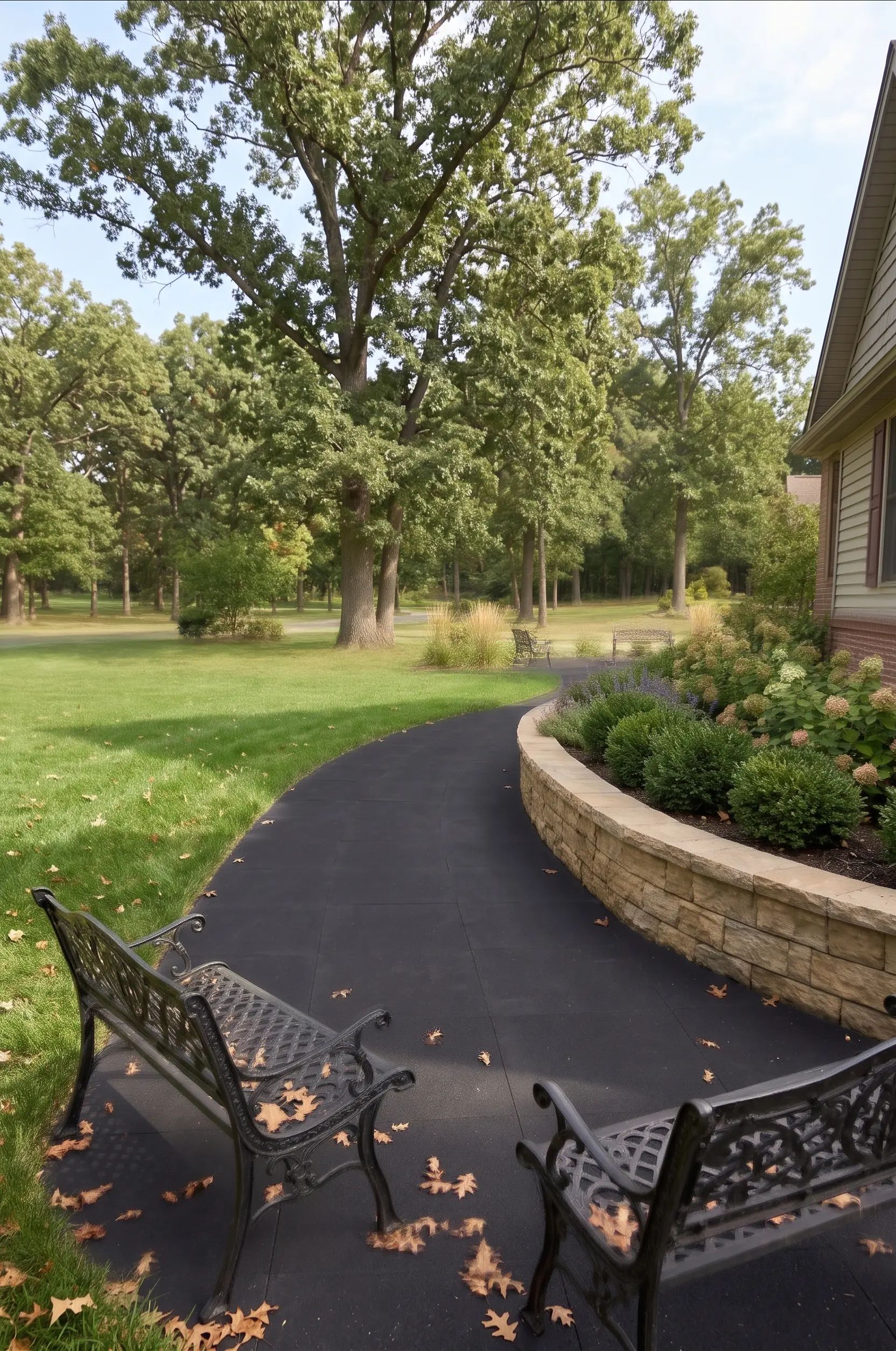 Curving black paved walkway bordered by a stone retaining wall with landscaping