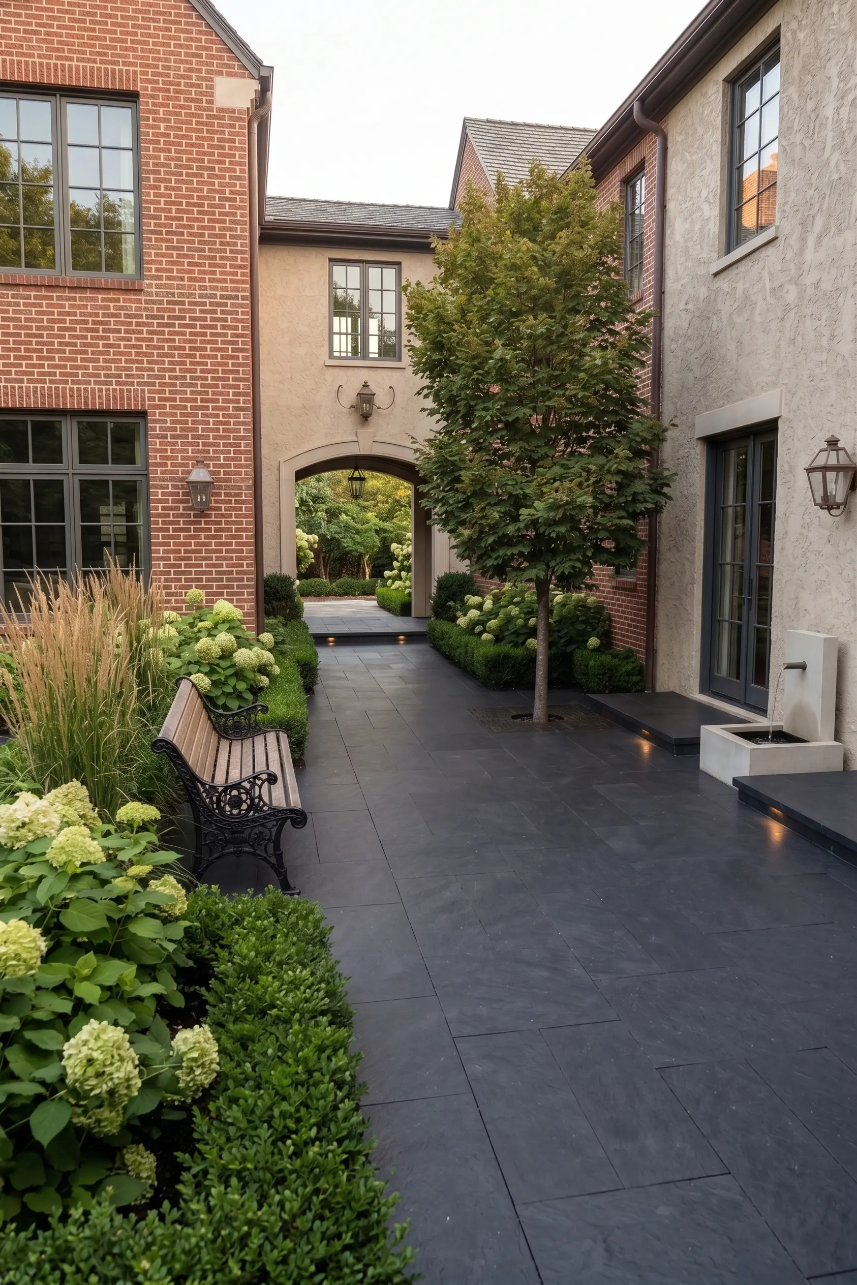 Basalt pavers form a pathway with manicured hedges and hydrangeas, leading to an arched entryway.