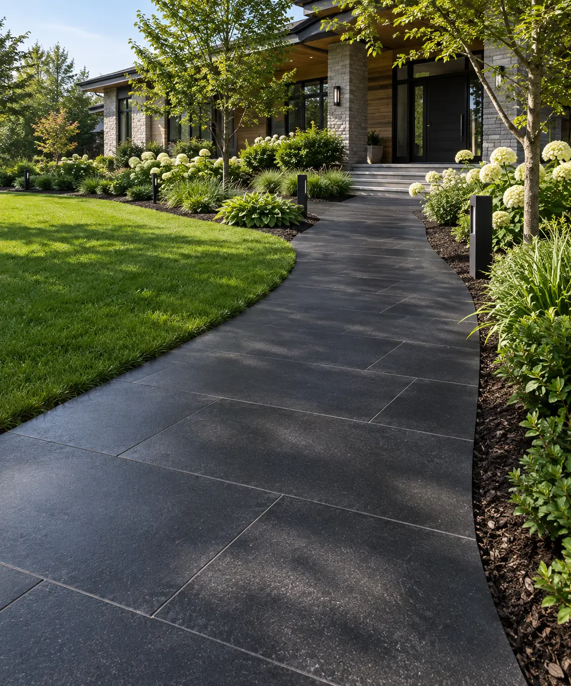 A curving pathway of large, dark granite stepping pavers leads to a modern home entrance.