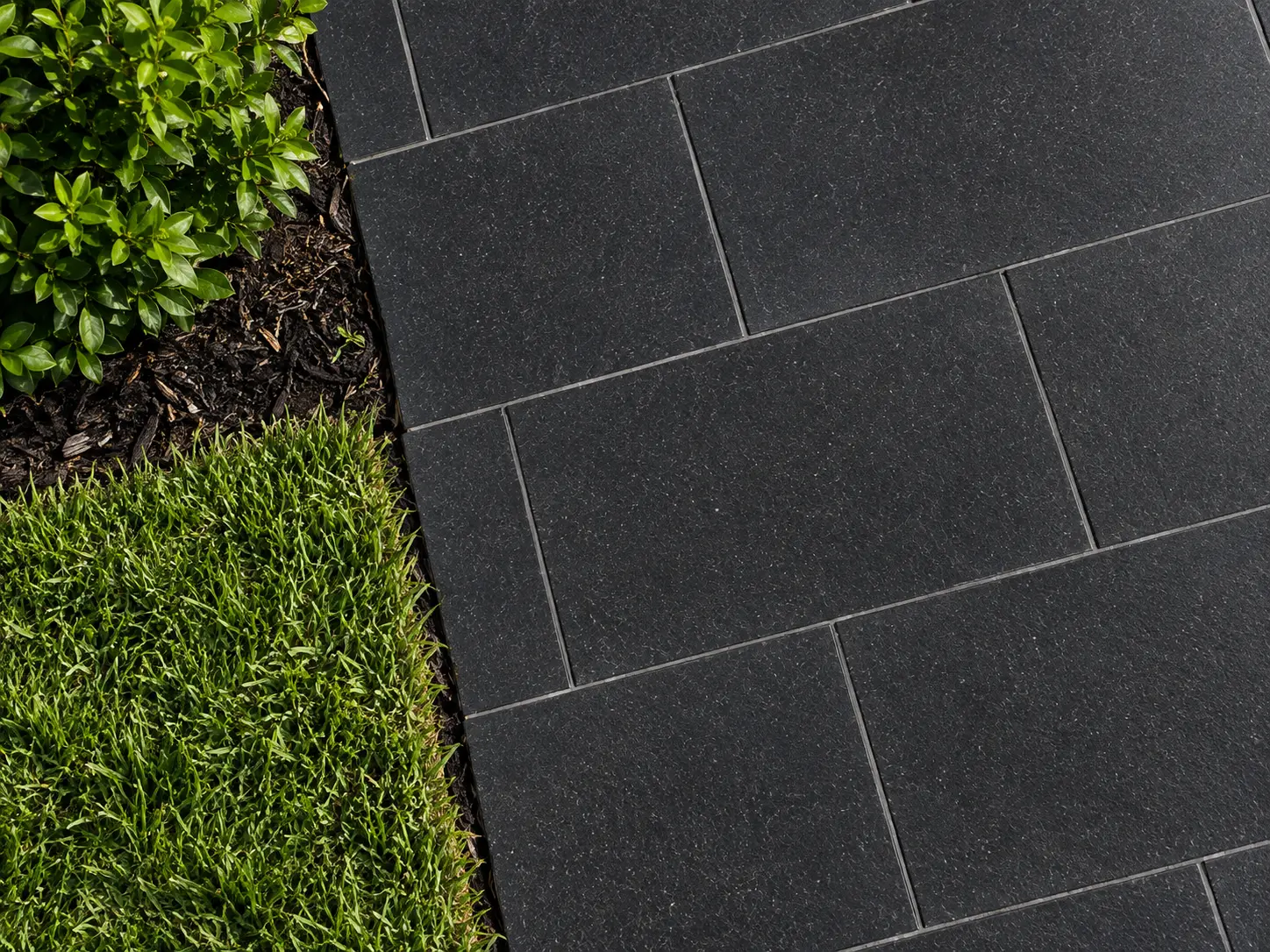 Dark Paver Stones Next to Grass Dark granite pavers with precise grout lines adjacent to lush green grass.