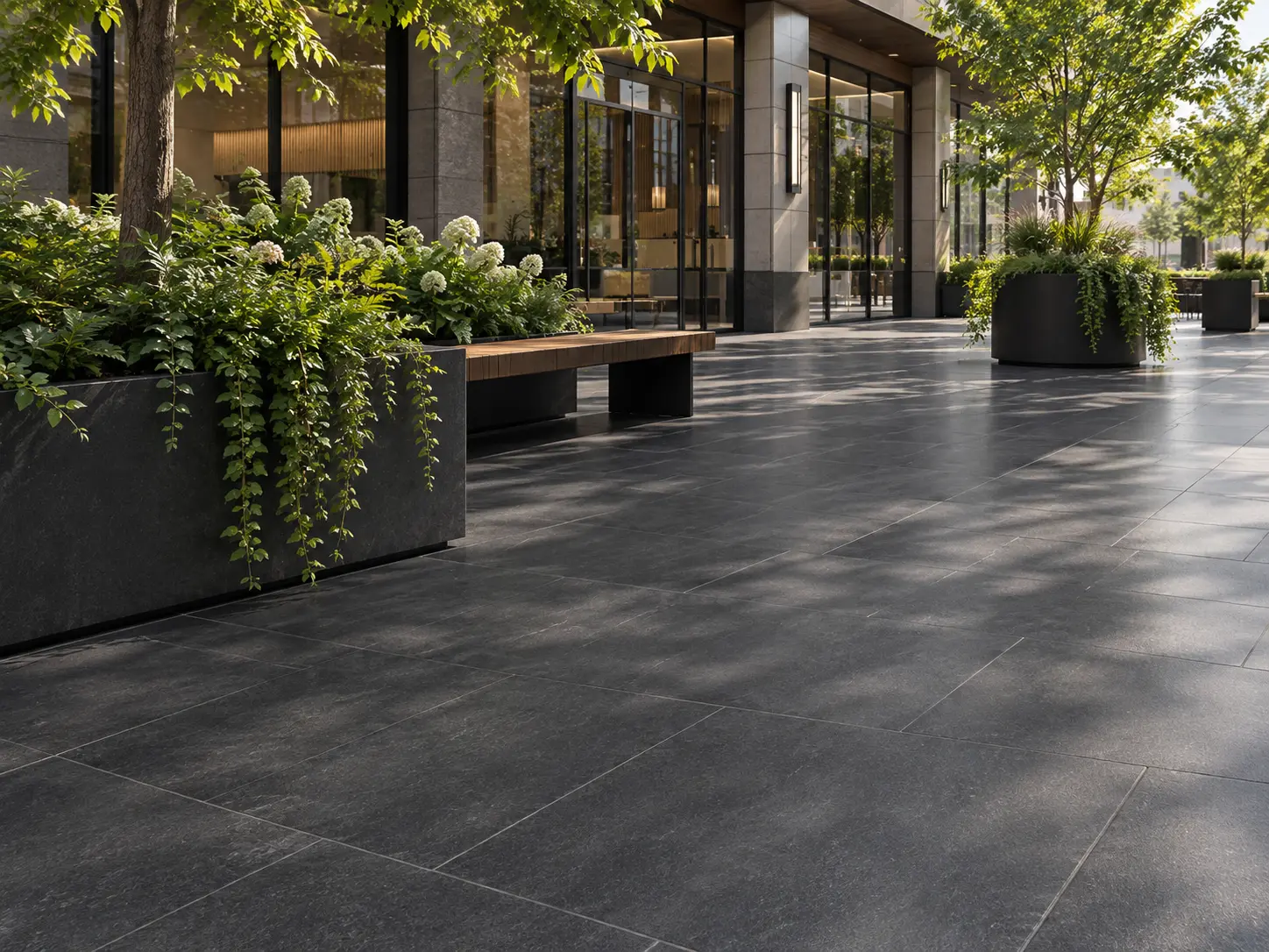 Dark Paving Stones with Plants Large, dark granite paving stones outside a building with planters and trees.