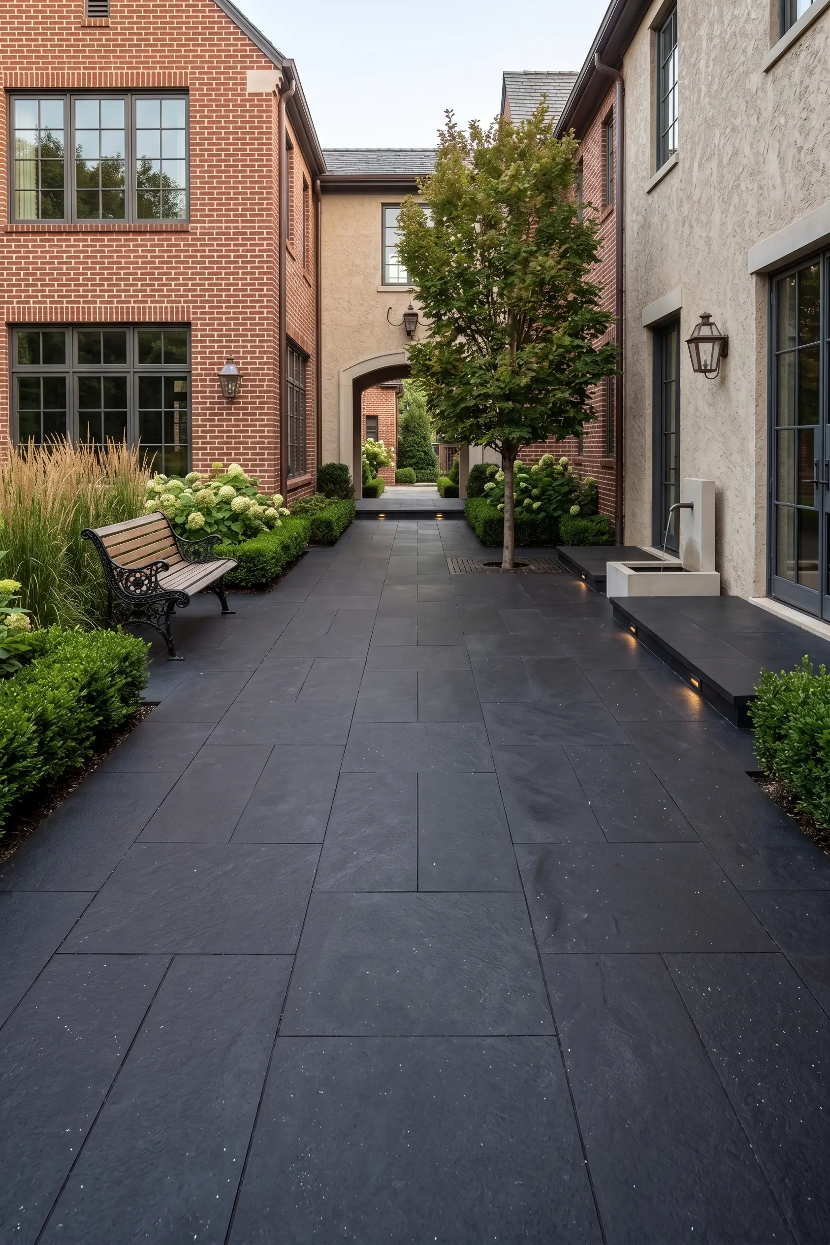 Dark stone patio and manicured garden Dark basalt hexagon tile patio with lush green landscaping and a bench