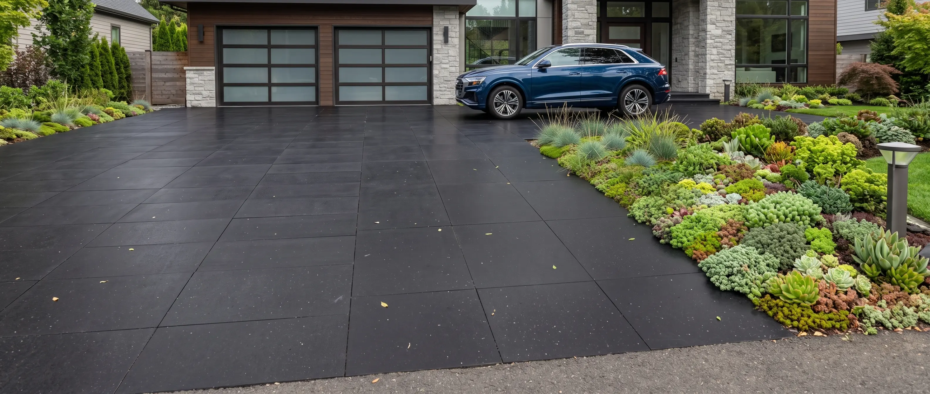 A blue SUV parked on a dark square-tile driveway next to a lush succulent garden.