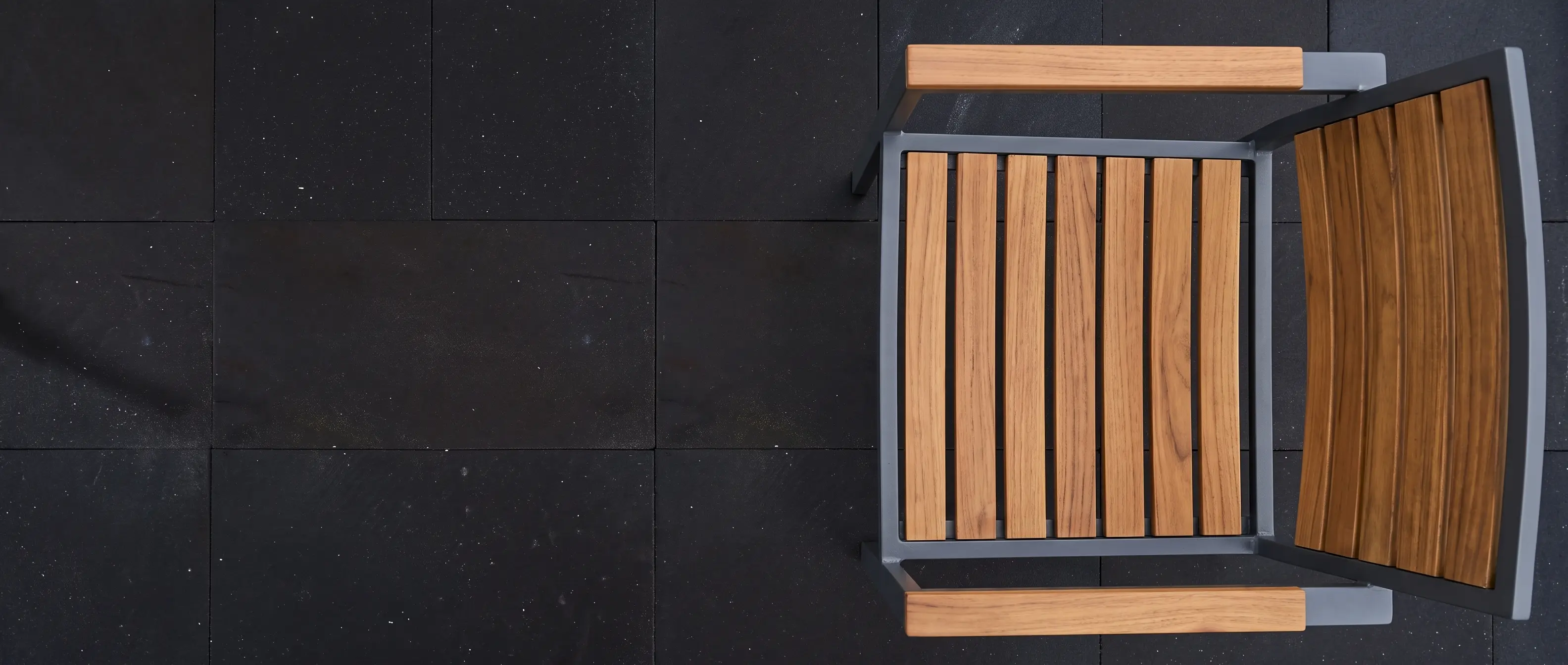A modern outdoor chair made of wood slats and metal sits on dark textured paving.
