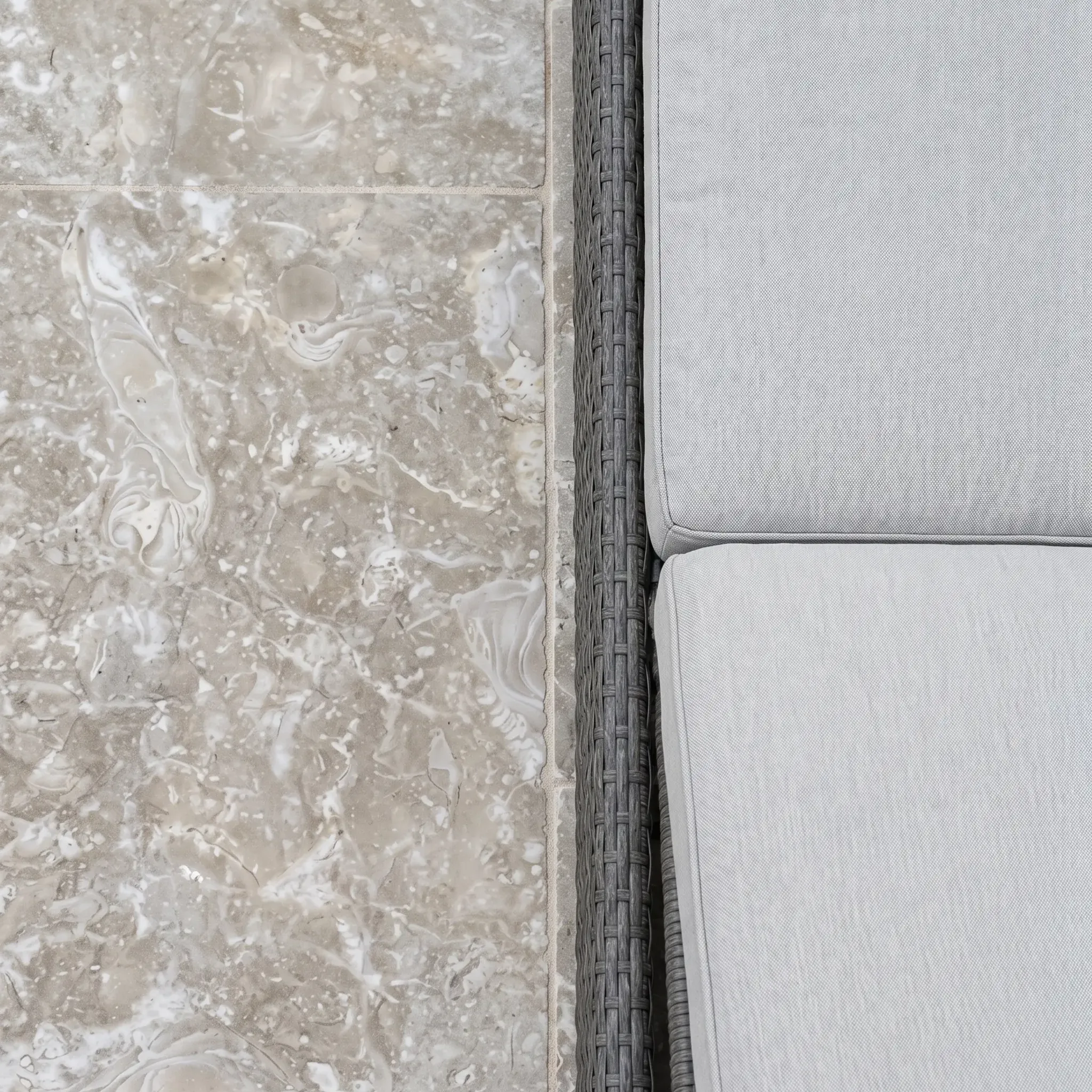 Top-down view of grey-beige fossil shellstone pavers next to a grey wicker sofa with light grey cushions.