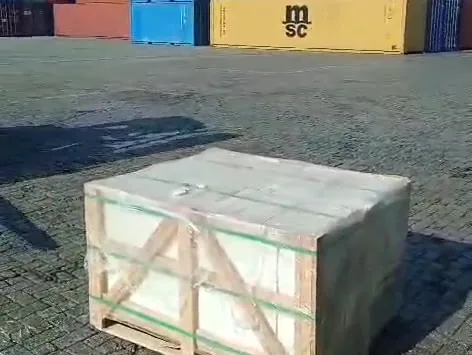 Film-wrapped crate on a port yard with stacked shipping containers behind.