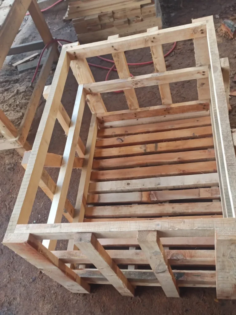 Empty long wooden crate frame with a heavy base, corner posts and slatted sides, in a workshop.