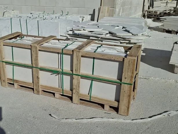 Long wooden crate in three bays holding stone slabs on edge, with green straps.