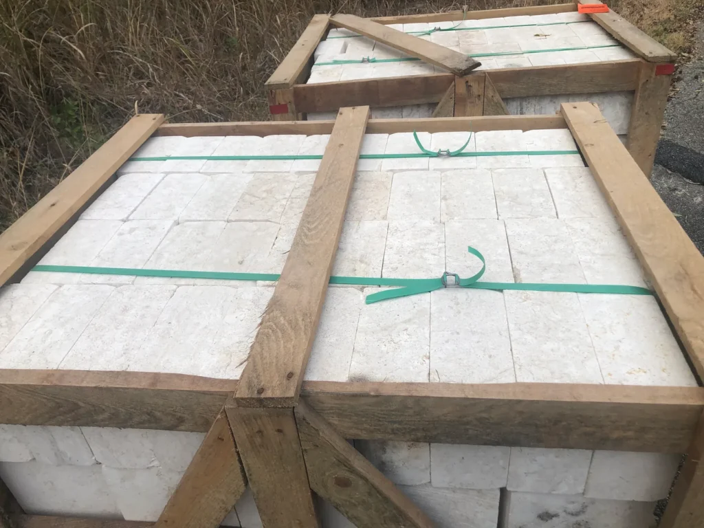Top of a crate showing white stone packed tight under wooden boards and straps.