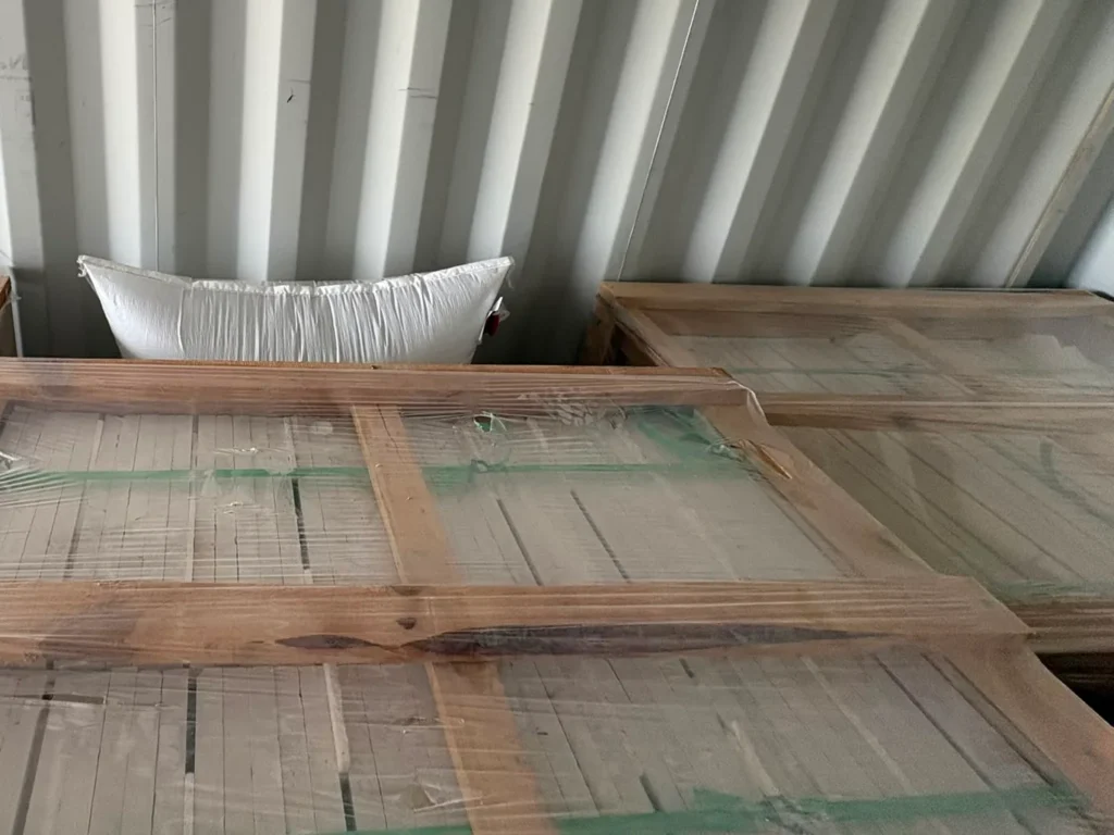 Tops of film-wrapped wooden crates inside a container, with a white air bag wedged between them.