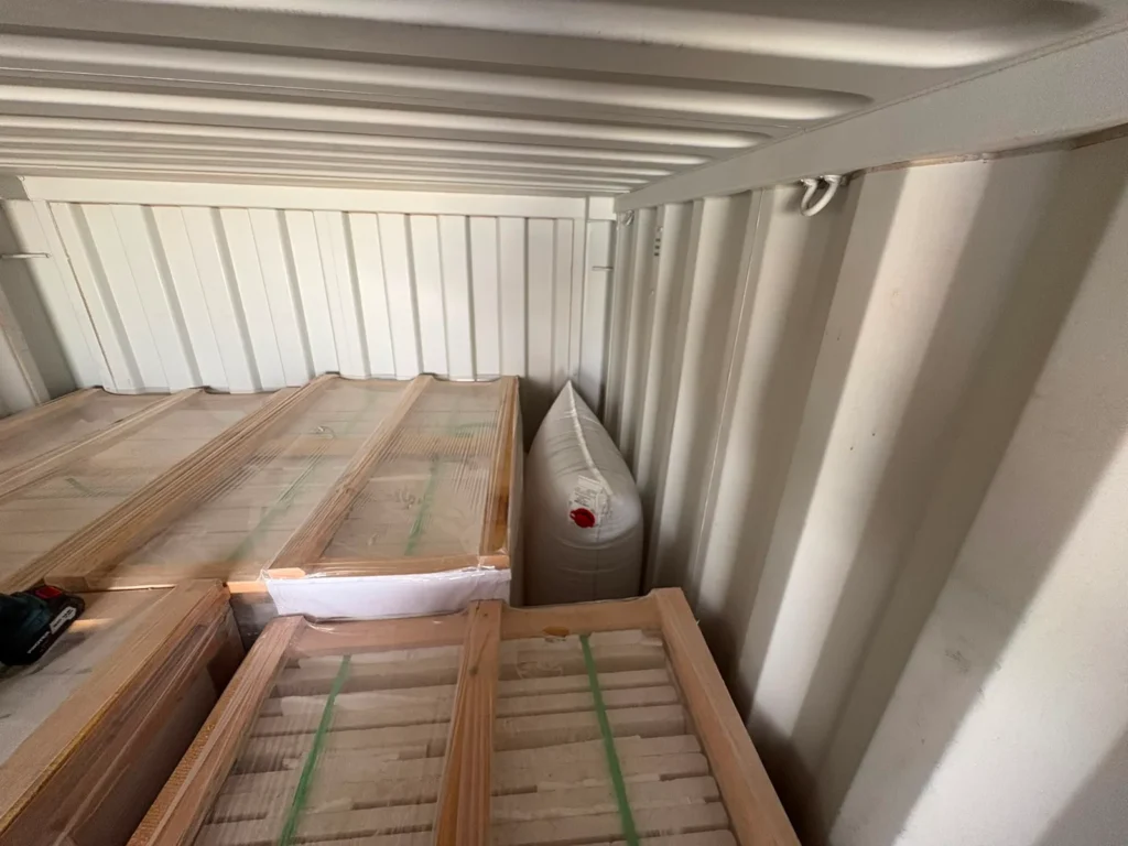 Film-wrapped wooden crates inside a container, with a white air bag standing upright between the crates and the wall.