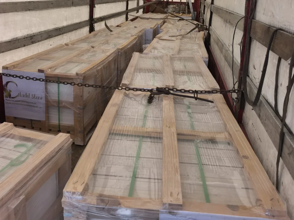 Long wooden crates inside a curtain-side truck, held down with a chain and a tensioner.