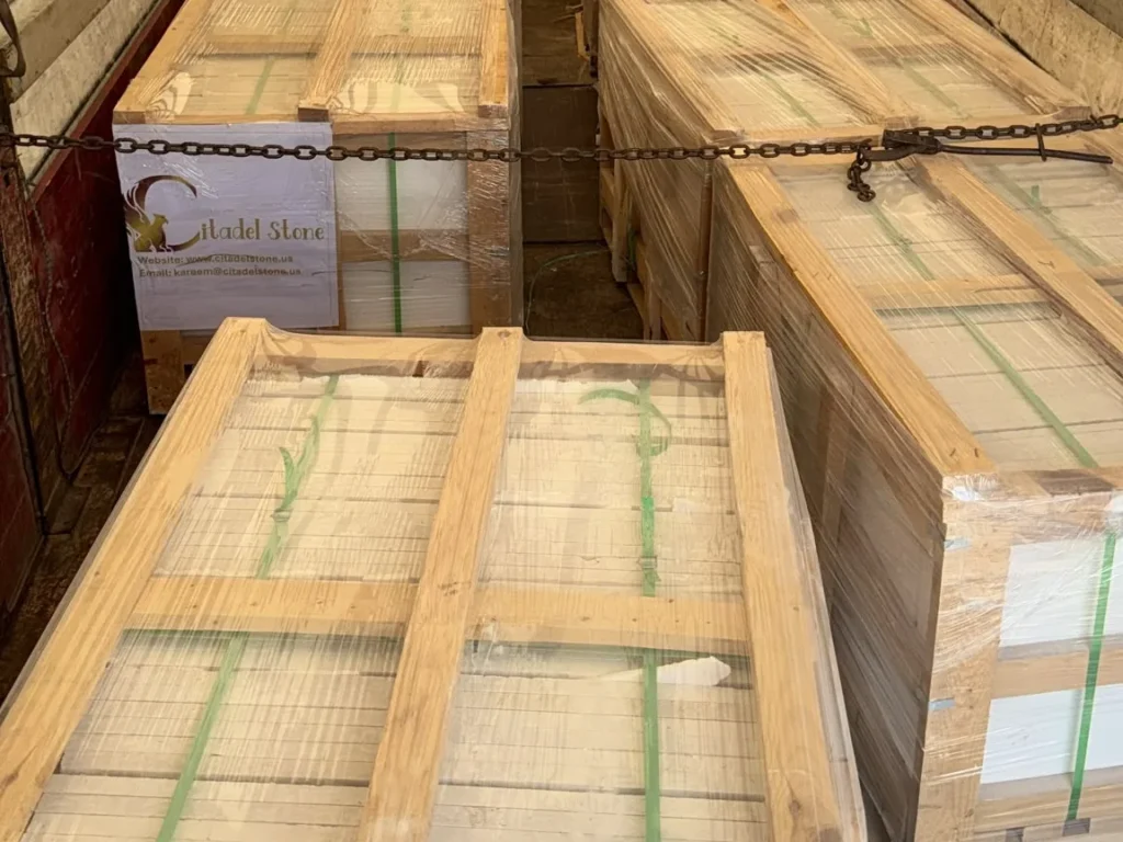Two rows of long wooden crates inside a curtain-side truck, held down with a chain.