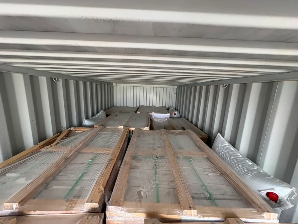 Inside a container: rows of wooden crates of stone, with white dunnage bags filling the gaps.