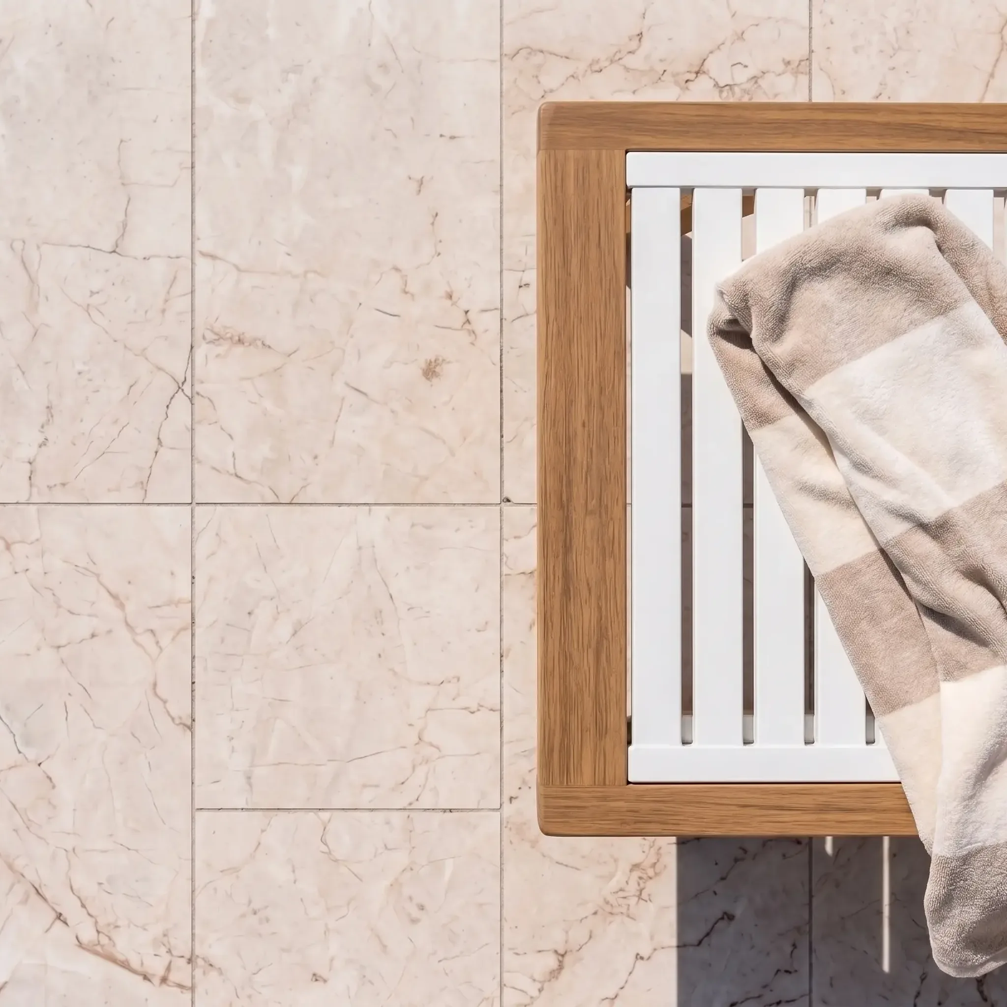 Overhead view of cream pink-veined limestone tiles with a teak-framed white lounger and a striped towel draped over it.