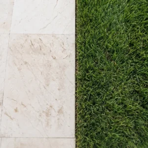 Close-up of light marble-look pavers with natural veining meeting a crisp, straight-edged lawn joint