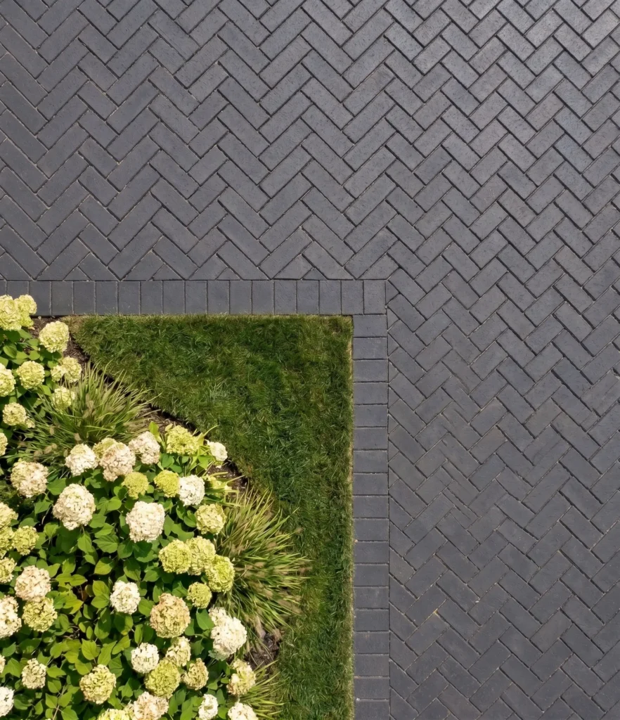 Dark grey cobblestone pavers in a herringbone pattern beside a lawn and flowering hydrangea border.