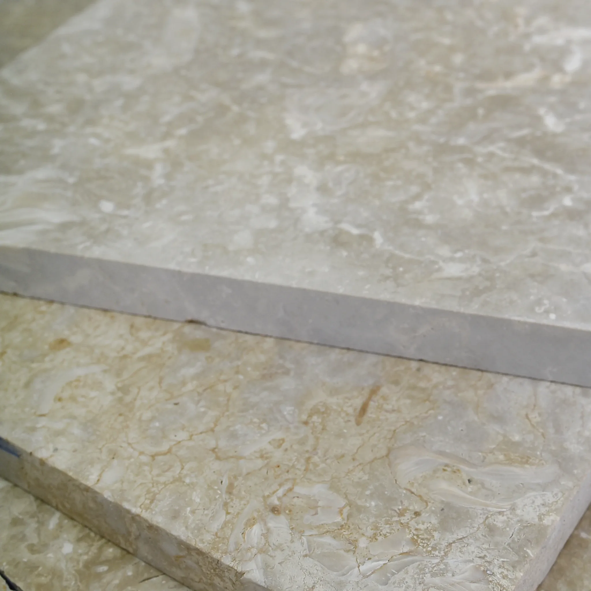 Two thick beige fossil shellstone pavers stacked offset, sawn edges showing thickness, on a tiled floor by a wood slat wall.