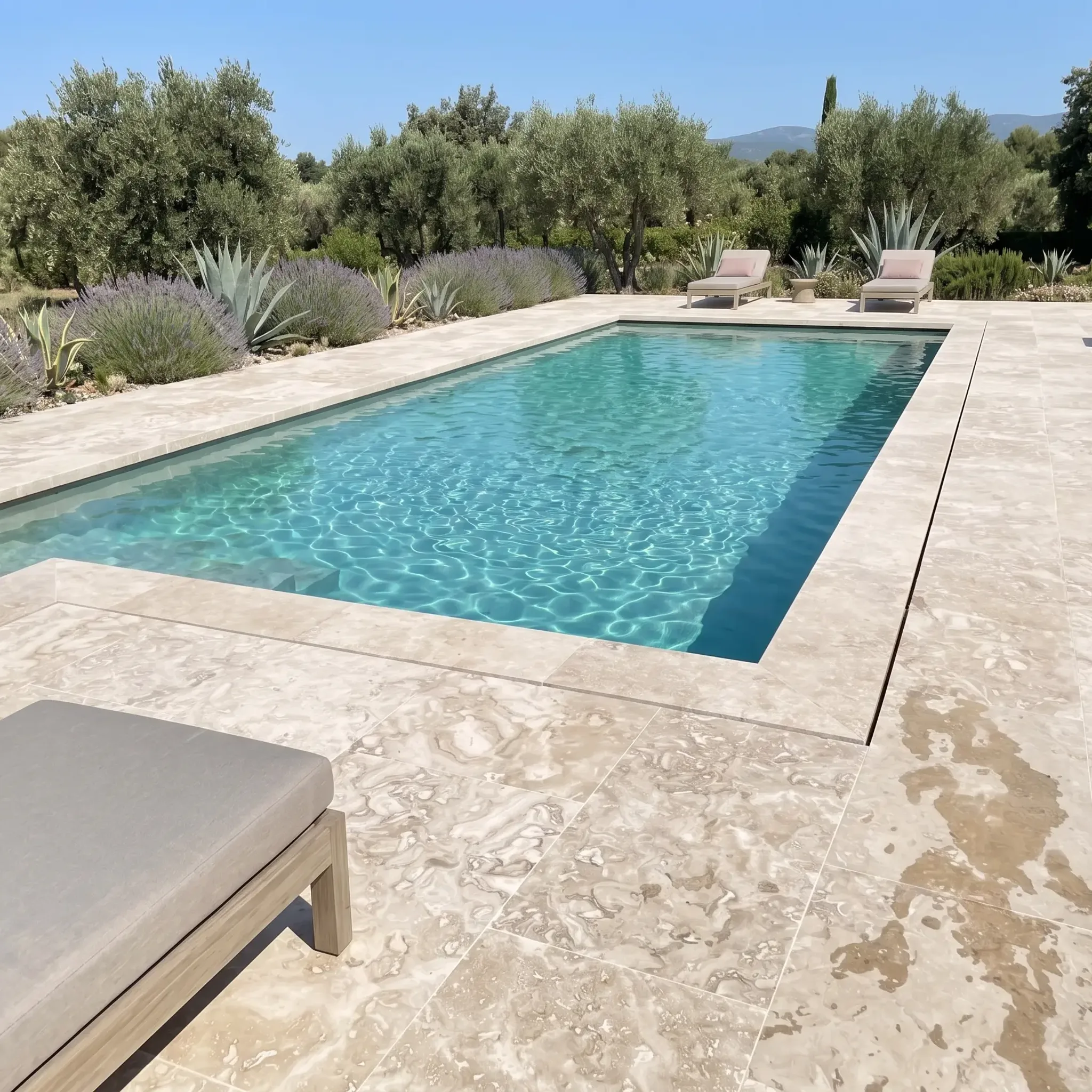 Beige honed travertine pool deck and coping with grey loungers, lavender and agave border, olive trees and mountains;…
