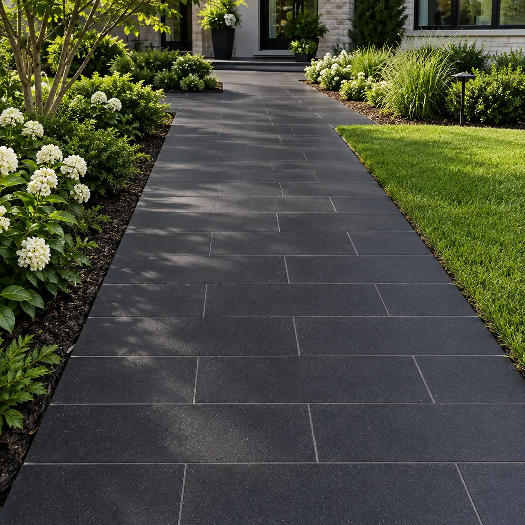 Walkway of charcoal plank-format basalt pavers in running bond to a modern house entry, white hydrangeas, lawn and…