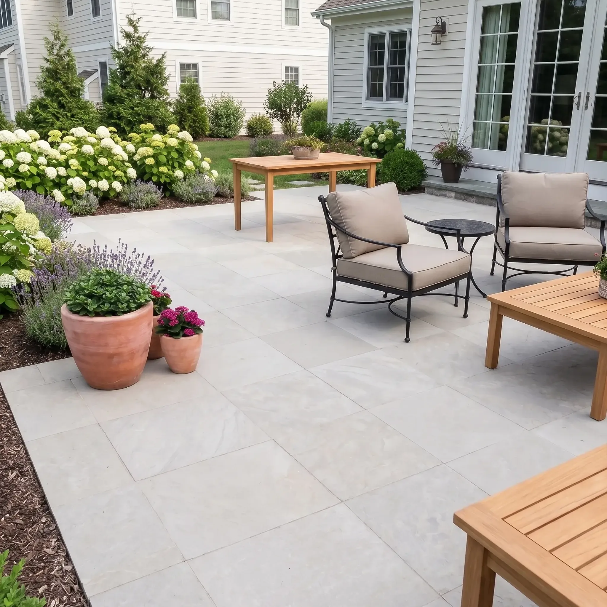 Pale grey limestone pavers on a patio with iron chairs, teak furniture, terracotta pots, hydrangeas and lavender by…