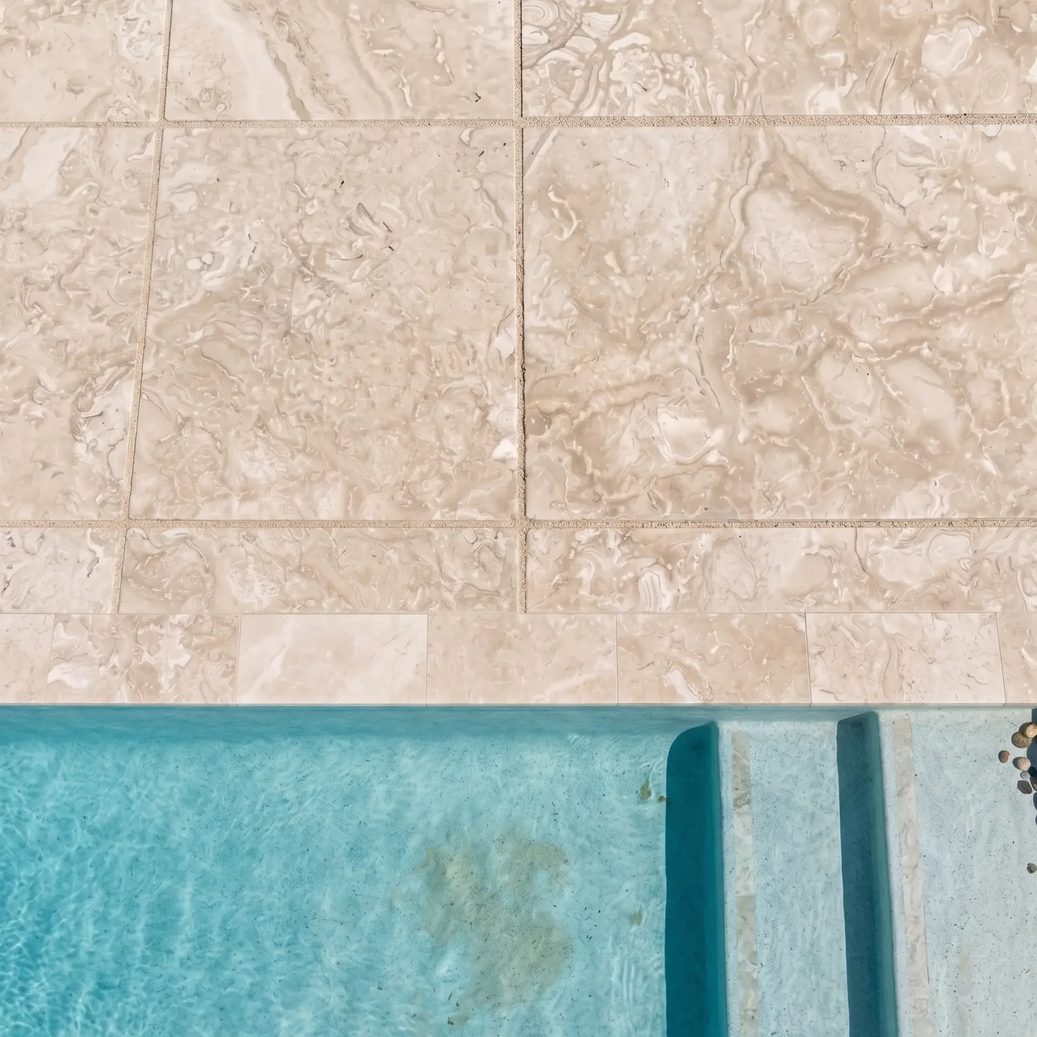 Top-down beige fossil limestone pavers with sand joints and bullnose coping at a turquoise pool with submerged steps.