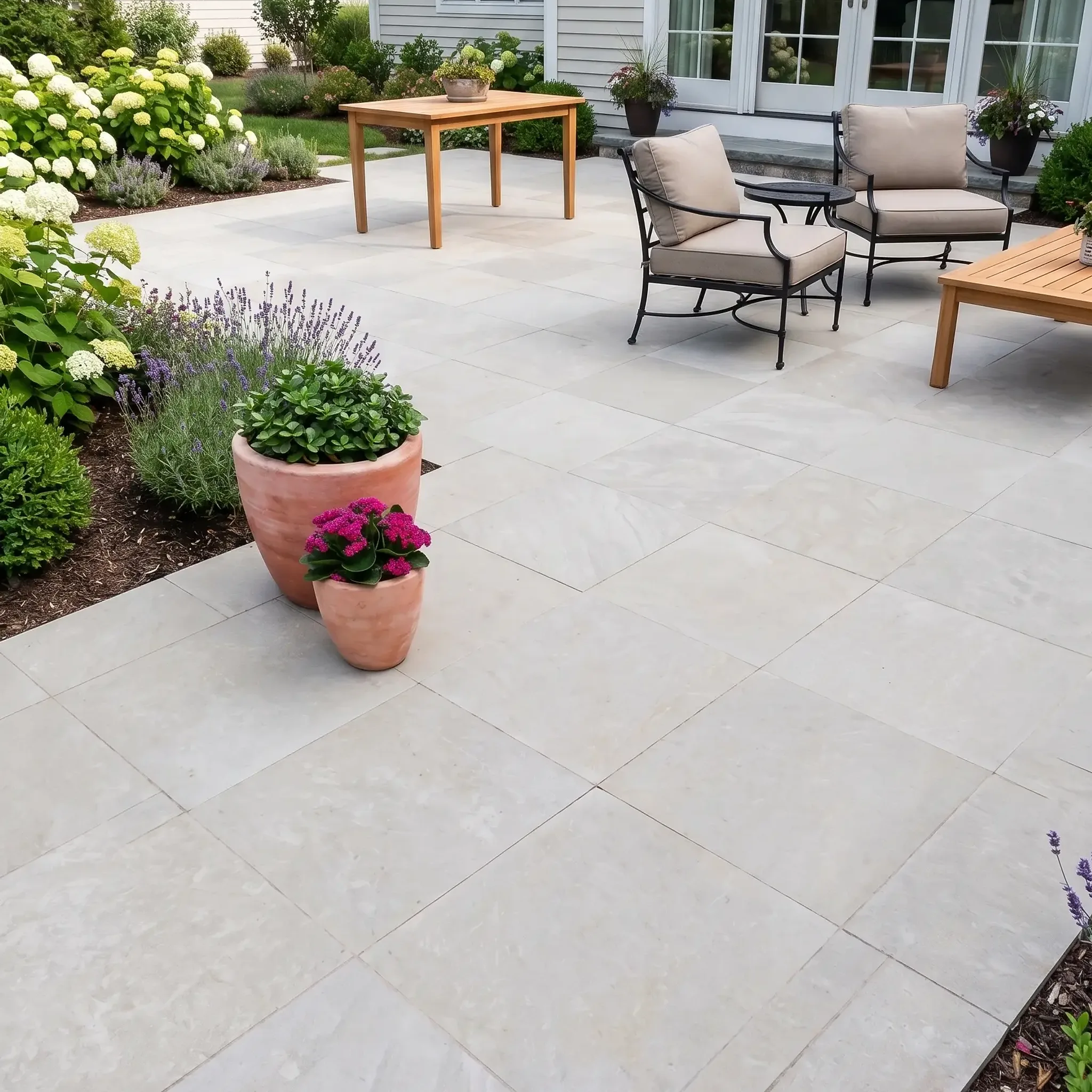 Pale grey large-format limestone pavers on a patio with teak table, iron armchairs, terracotta pots and French doors.
