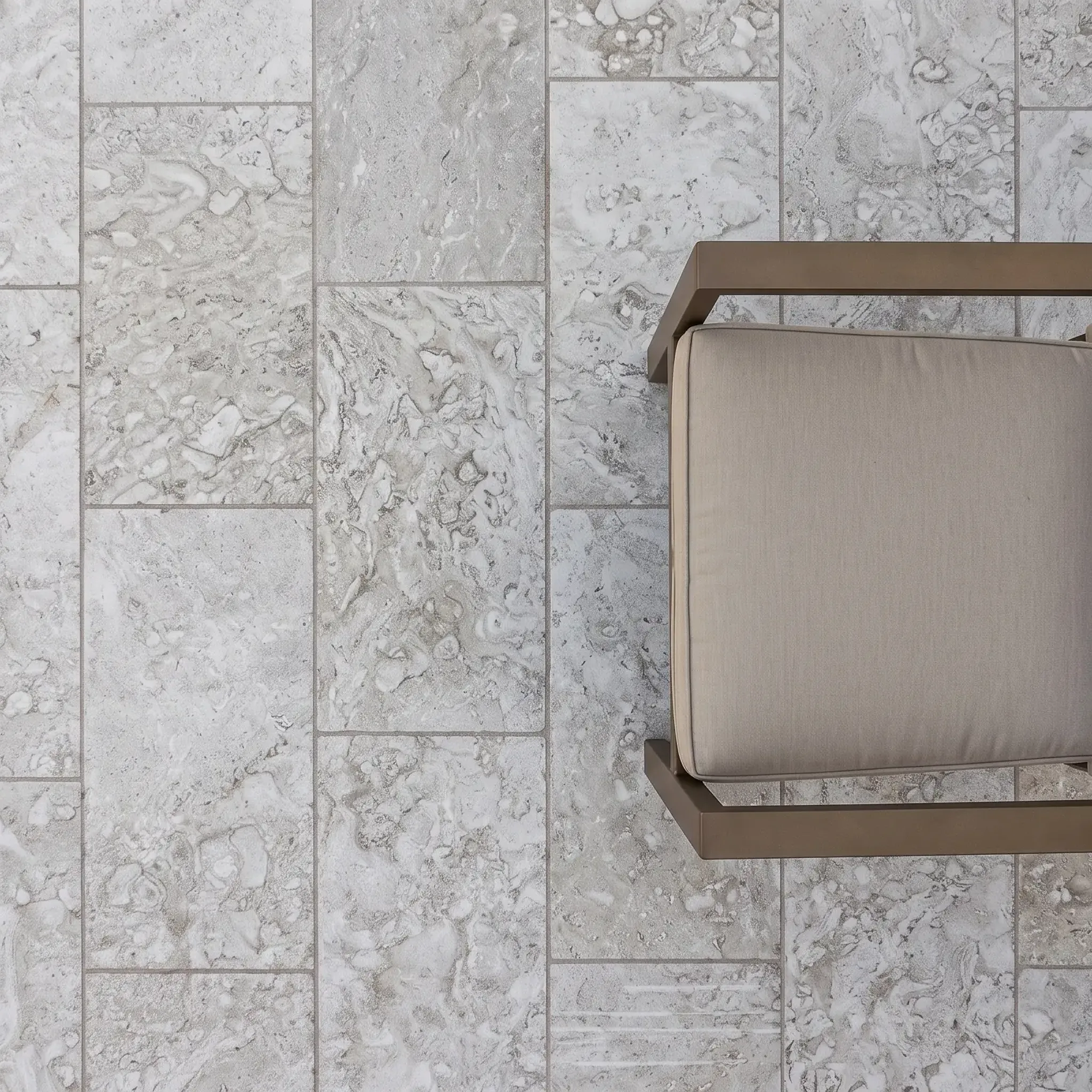 Top-down view of grey-white mottled shellstone pavers in running bond with a bronze-framed patio chair and beige cushion.