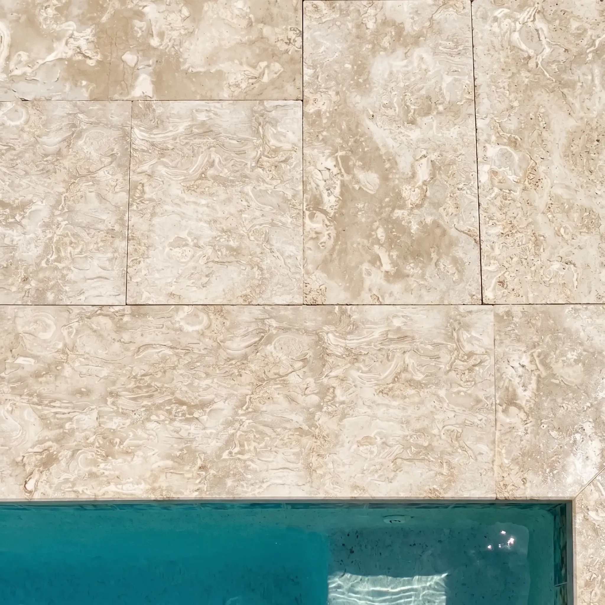 Top-down view of beige fossil shellstone pavers and a coping edge meeting turquoise pool water.